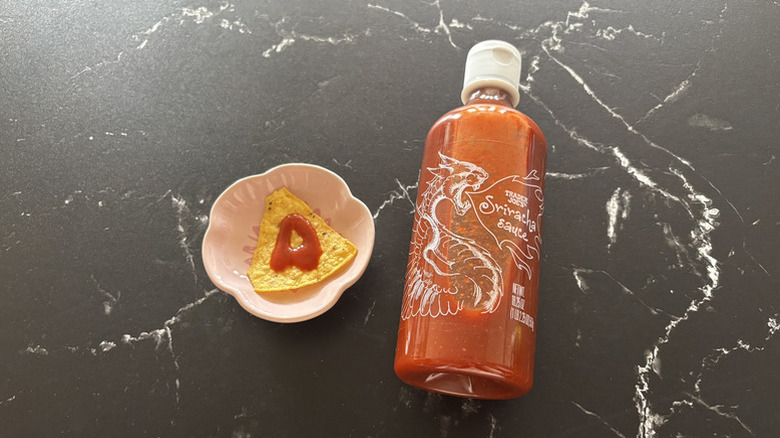 bottle of Trader Joe's Sriracha Sauce next to a tortilla chip with a dab of sauce on it