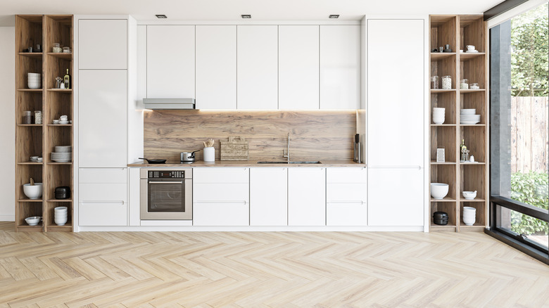 Shot of white kitchen surrounded by wood shelving units, herringbone patterned wood floor