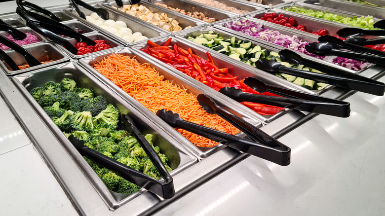 salad ingredients in metal containers with black tongs at salad bar