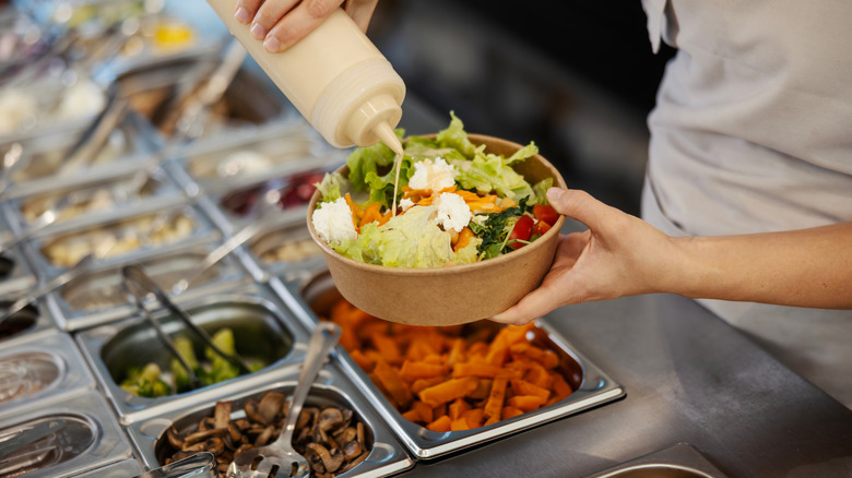 person dressing salad at salad bar
