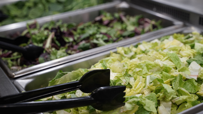 metal containers of lettuce with black tongs at salad bar