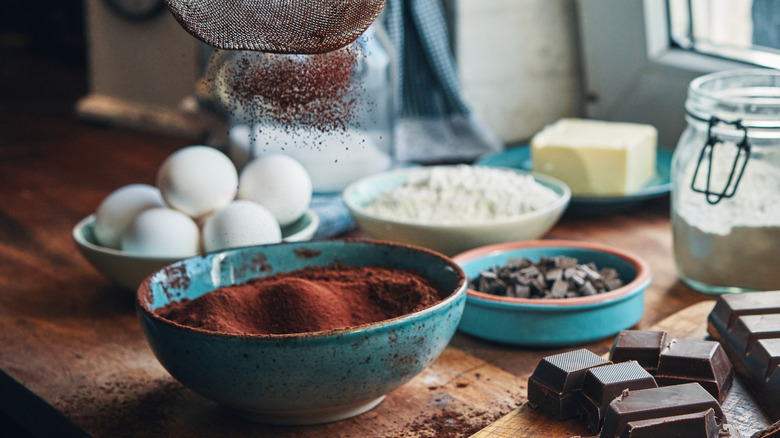 Baking still life with bowl of cacao, chocolate bar, eggs, and flour on rustic wooden table