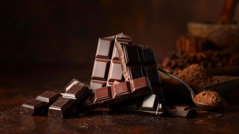 Chocolate arranged sculpturally on dark surface with spoon of cocoa powder