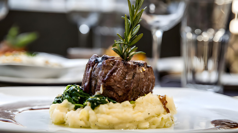 A filet mignon steak on creamy mashed potatoes on a plate.