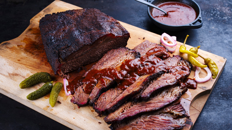 Smoked wagyu beef brisket served with vegetable on a wooden cutting board.