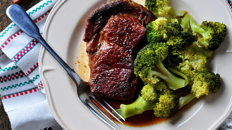 A grilled ribeye steak with boiled broccoli on a plate.