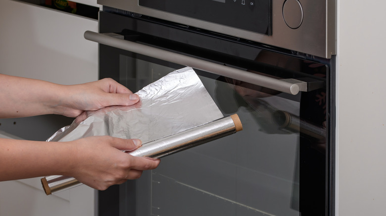 hands rolling out tin foil with oven door in background
