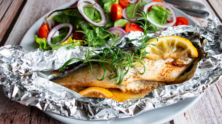 baked fish with lemons and herbs in open foil packet on plate with salad