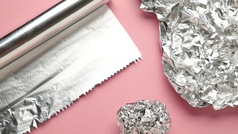 roll of tin foil with crumbled pieces on pink background