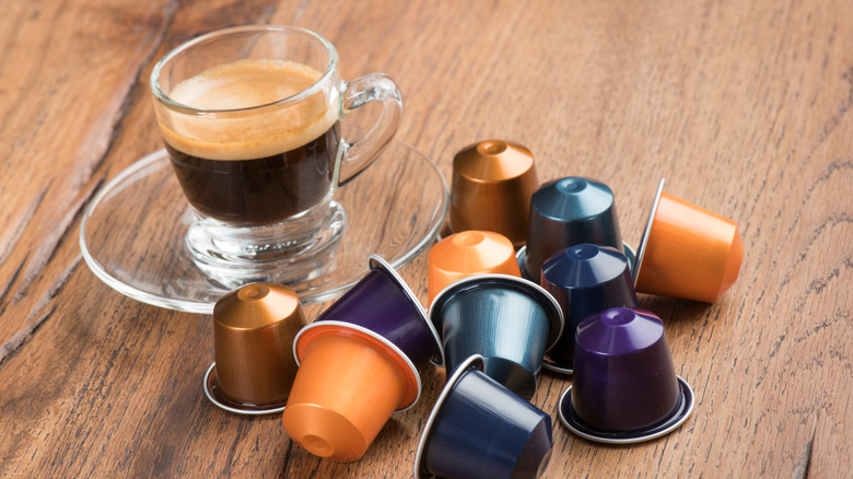 A glass cup of Nespresso with various pods next to it on a wooden counter