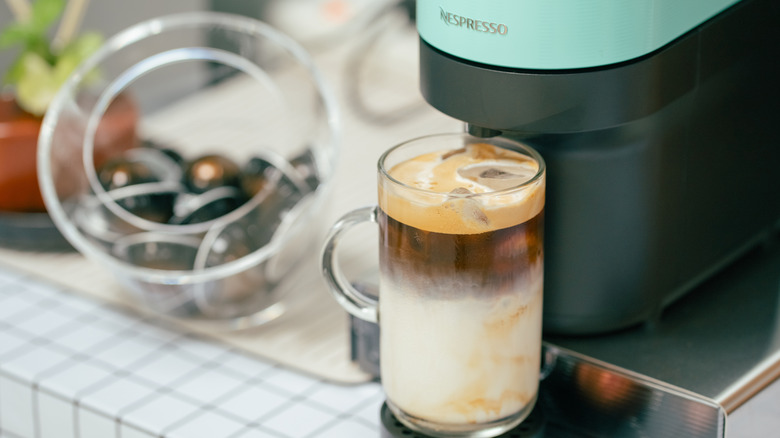 A Vertuo Pop+ machine brews a latte with a bowl of Vertuo pods next to it