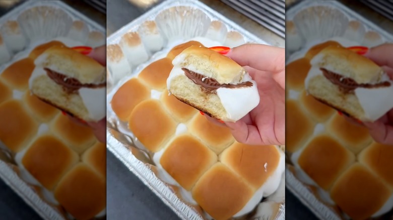 Hand pulling a s'more sandwich out of a metal tray