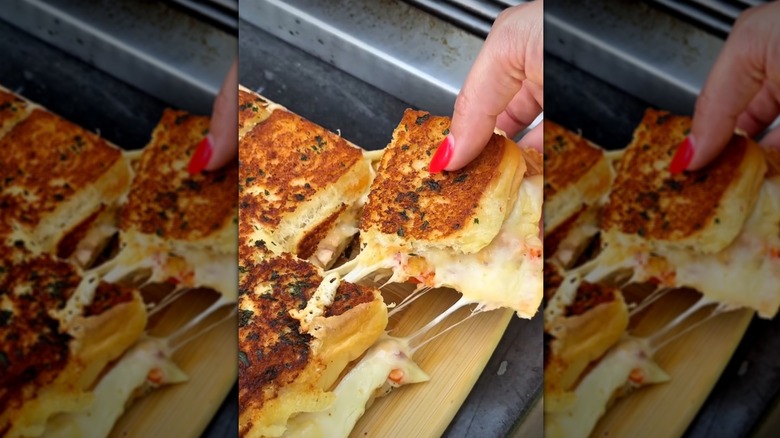 Hand pulling grilled cheese slider from a wooden board
