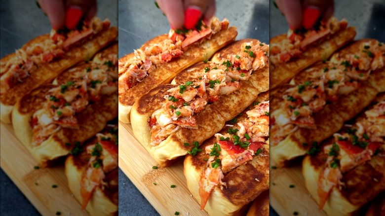 Hand sprinkling herbs onto lobster rolls on King's Hawaiian rolls