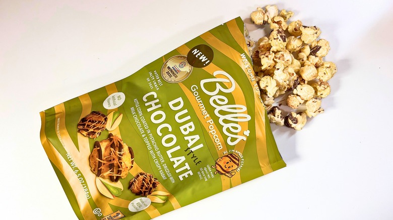 Popcorn spilling out of bag of Belle's Dubai Chocolate popcorn onto white table