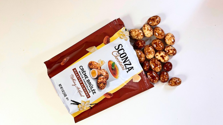 Almonds spilling out of bag of Sconza Crème Brûlée White Chocolate Roasted Almonds onto white table