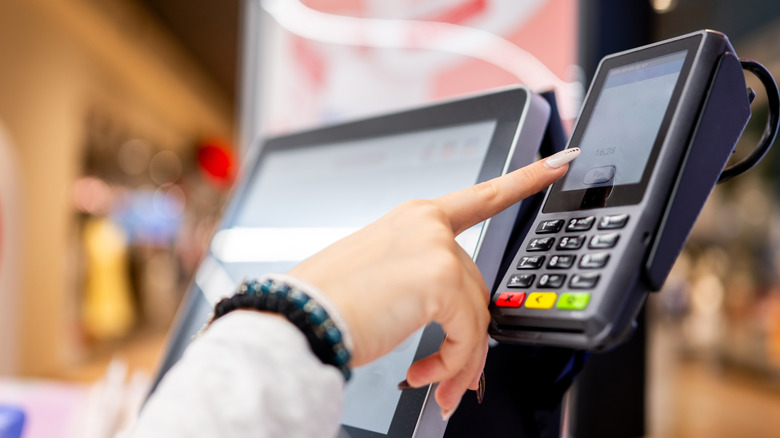 A person's hand pressing buttons at self checkout station