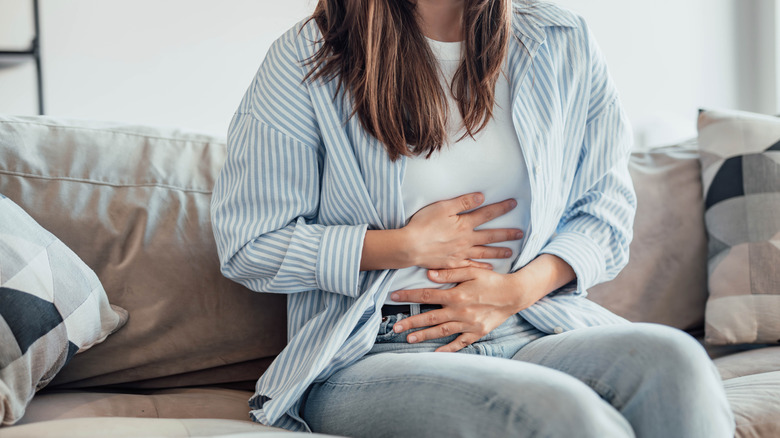 woman sat on sofa holding belly