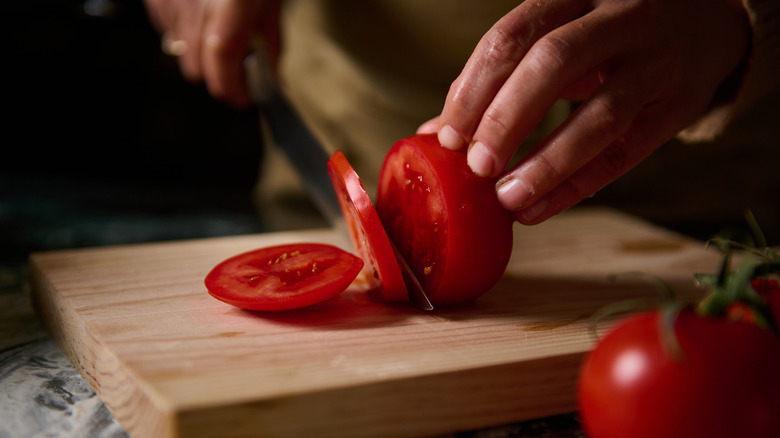Close-up of hands slicing juicy red tomatoes on a wooden cutting board