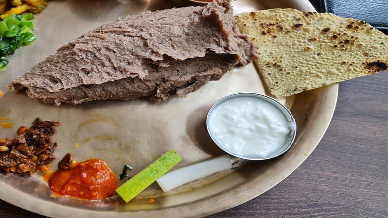 Traditional Nepali dhido on plate with vegetables, bread, and dips