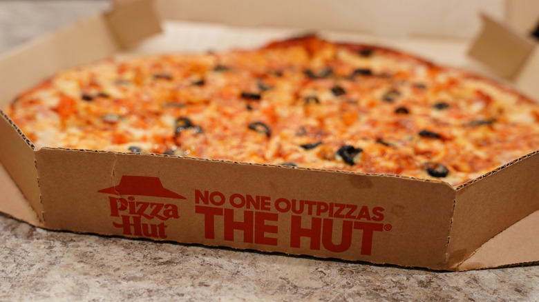 Cooked Pizza Hut thin crust pizza in a delivery box on kitchen counter