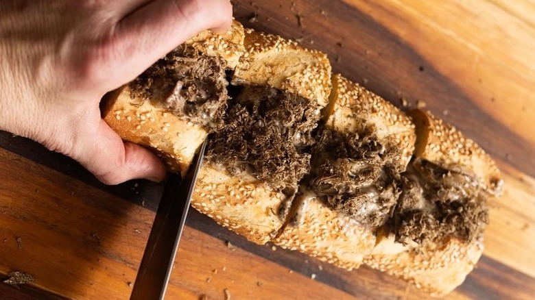 Hand cutting slices of a Barclay Prime cheesesteak
