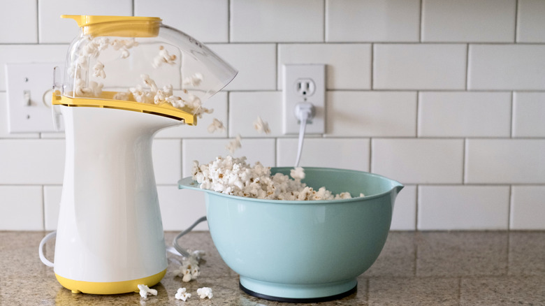 Hot air popcorn maker in yellow and white, with a blue bowl collecting the popcorn