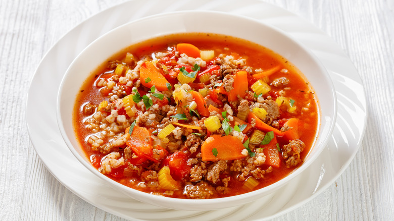 Hamburger soup with vegetables in a white bowl on a white table