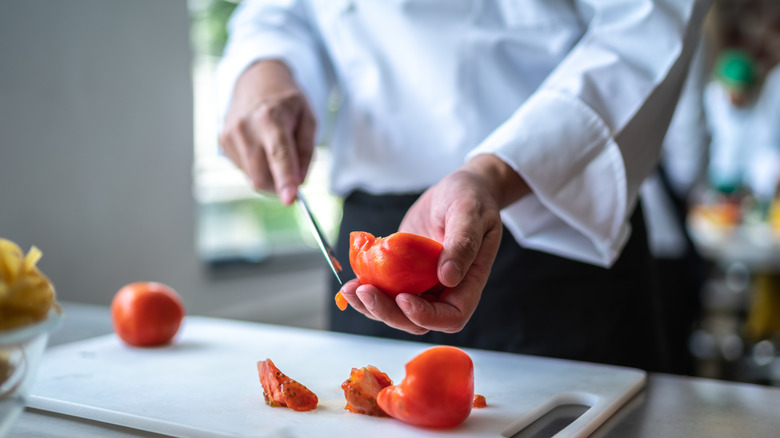 Close up of chef chopping a tomato in a commercial kitchen