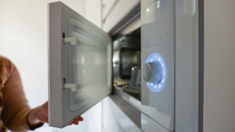 A person's hand opens the door of a sleek, contemporary microwave oven