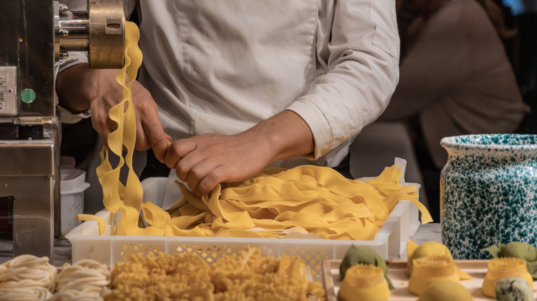 Chef creating fresh tagliatelle pasta by hand from a pasta machine