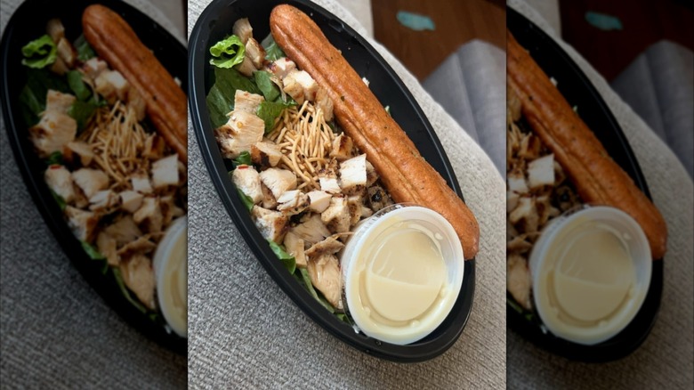 Small salad with breadstick in takeout container on grey cushion, mirrored image