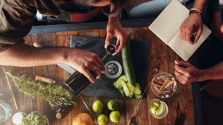 Top down view of two barmen creating a cocktail and taking notes.