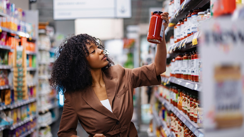 Woman picking up jar of pasta sauce to examine label in grocery store