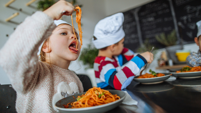 Young girl with chef hat putting fork full of spaghetti into her mouth