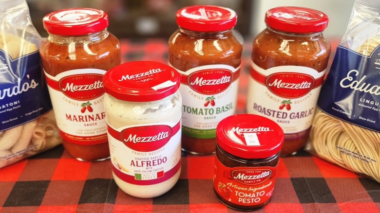 Four jars of Mezzetta pasta sauce in different flavors, along with jar of tomato pesto and two bags of dry pasta on table