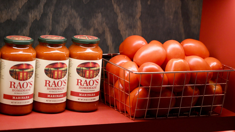 Three jars of Rao's Homemade marinara sauce on shelf beside wire basket full of tomatoes
