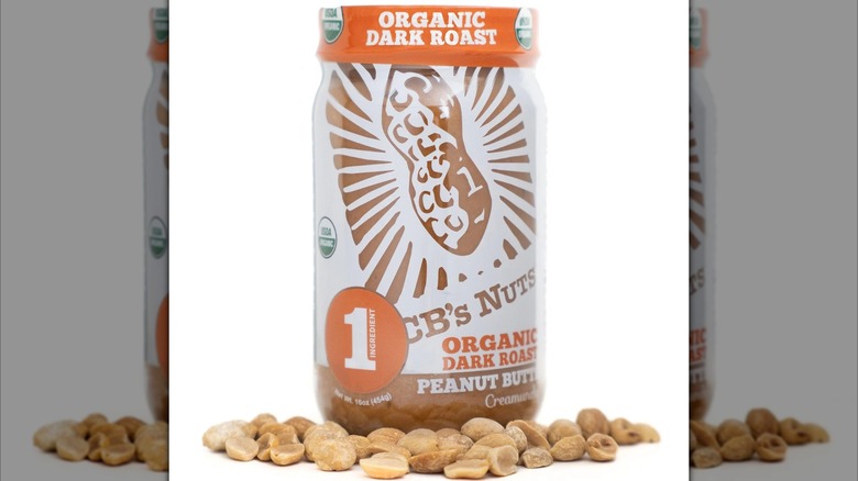 Jar of CB's Nuts Organic Dark Roast Peanut Butter surrounded by shelled, roasted peanuts