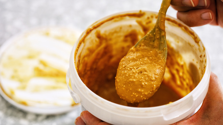 Hand scooping crunchy peanut butter out of pail with spoon