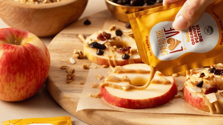 Hand squeezing peanut butter onto apple slices from single-serving packet