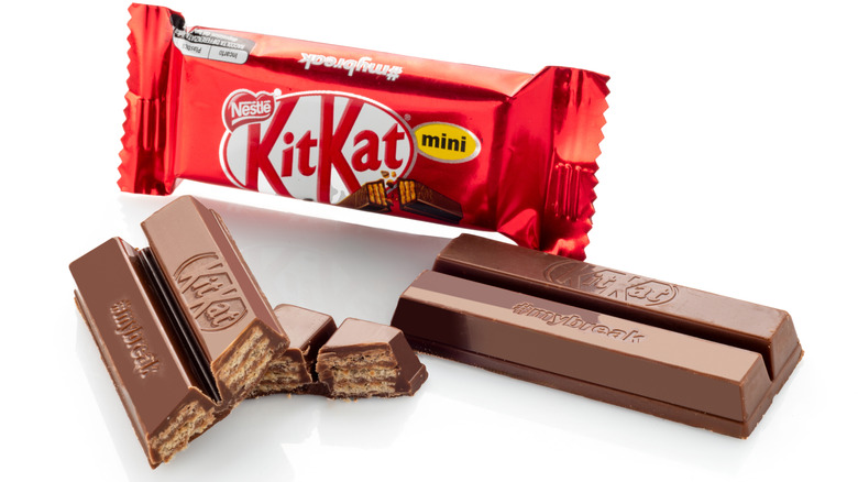 Broken Kit Kat bar next to a Kit Kat wrapper on a white background