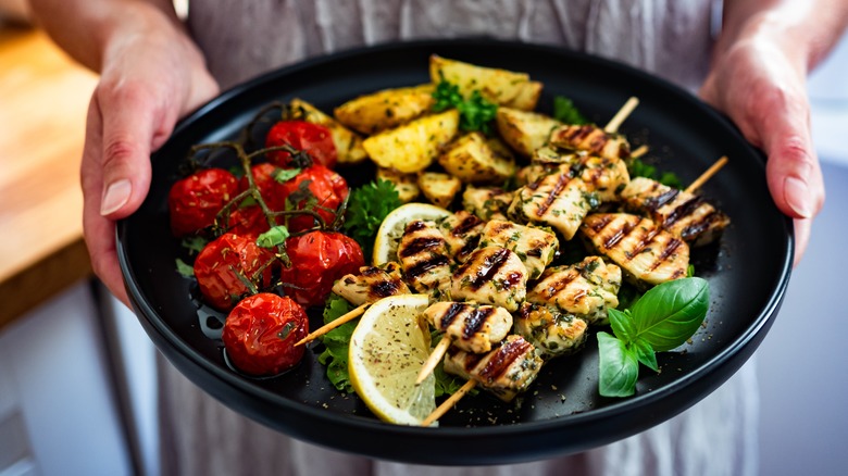 woman holds plate with vegetables and souvlaki