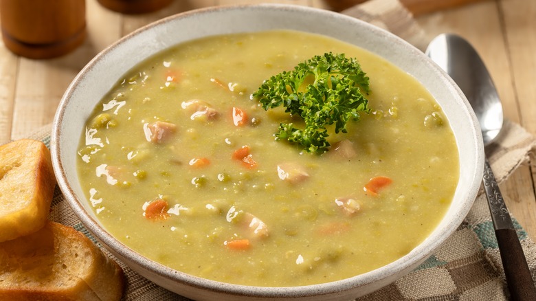 white bowl of split pea soup on table with bread and spoon