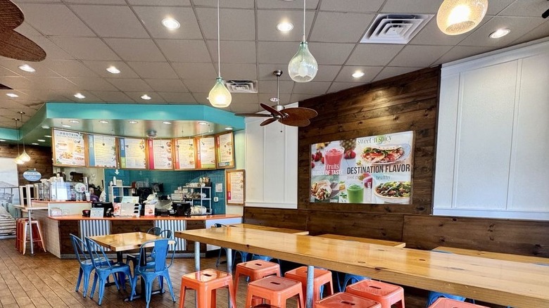 Seating area of Tropical Smoothie Cafe in front of ordering counter, with pictures of menu items throughout shop