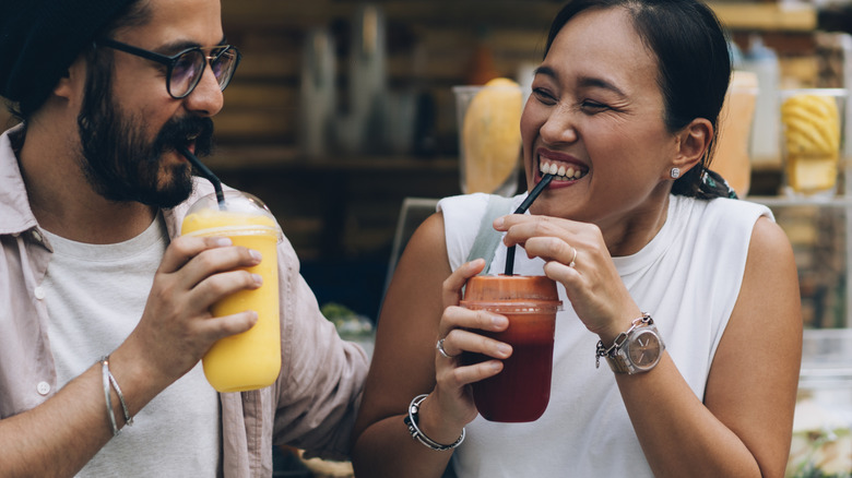 Young couple smiling and sipping smoothies from plastic cups