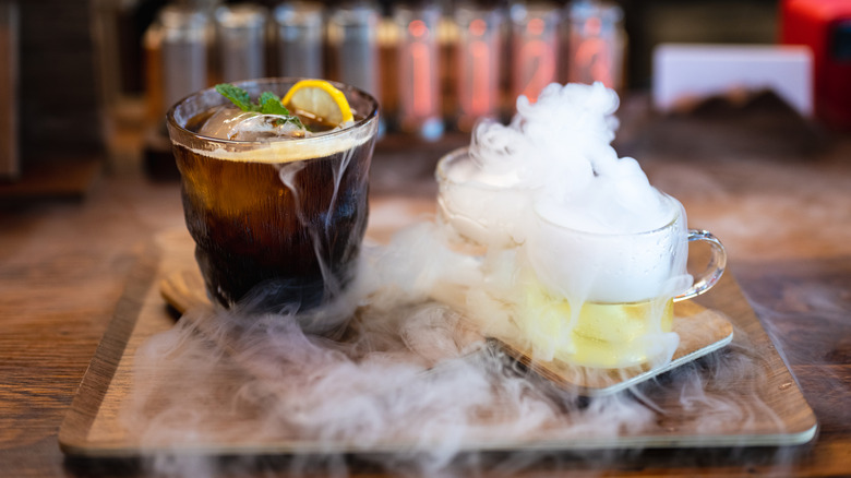 A cup of Americano with ice cubes, lemon slices and mint, and dry ice