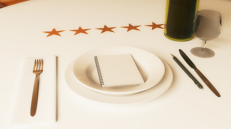 Restaurant rating concept. Dining table with wine, cutlery, spiral notepad and five stars.
