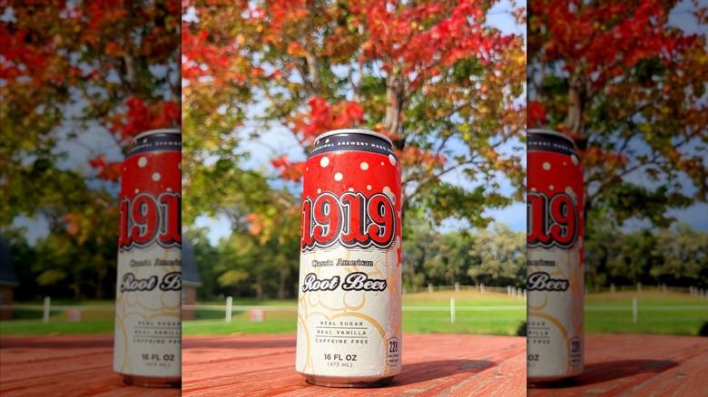 Can of 1919 Root Beer on a wooden table in front of trees during the fall