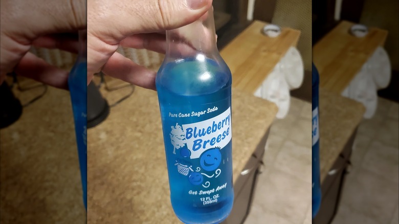 Hand holding a glass bottle of bright blue Blueberry Breese soda