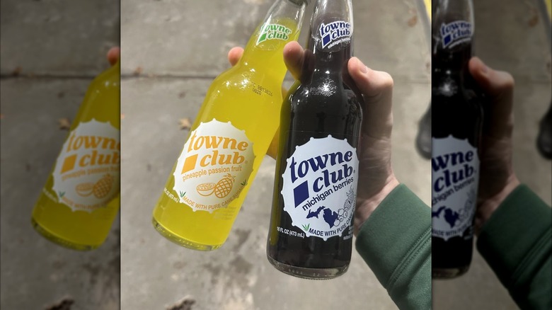 Hand holding glass bottles of pineapple passion fruit and Michigan berries Towne Club sodas